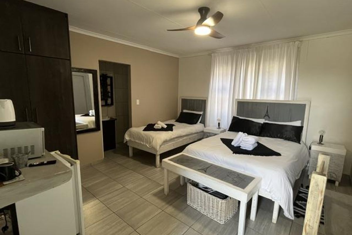 A well-maintained bedroom featuring tiled flooring, built-in cupboards, and a ceiling fan, with an adjoining en-suite bathroom area.
