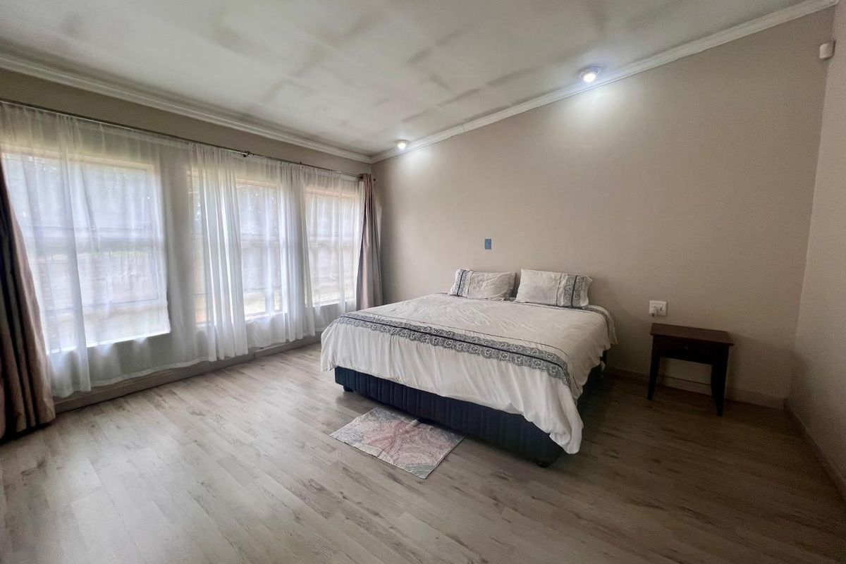 A spacious bedroom featuring light-toned wood-look flooring, large windows with sheer curtains, and recessed ceiling lighting.