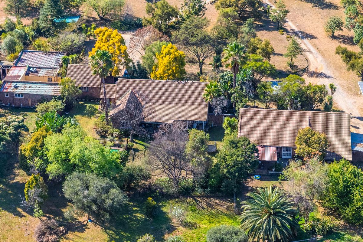 Aerial view of a small holding property featuring multiple buildings with tiled roofs, a swimming pool, and extensive mature garden grounds.