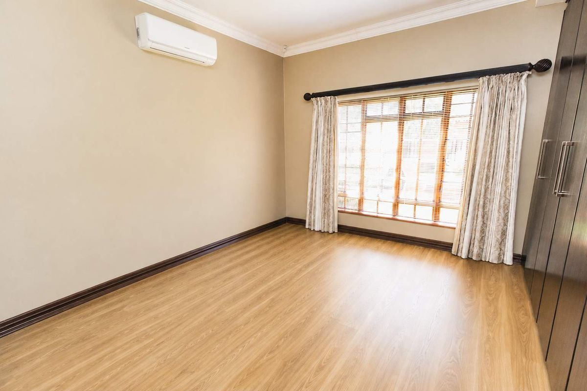 A bright, empty bedroom featuring light wood-look flooring, built-in dark cabinetry, and a wall-mounted air conditioning unit.
