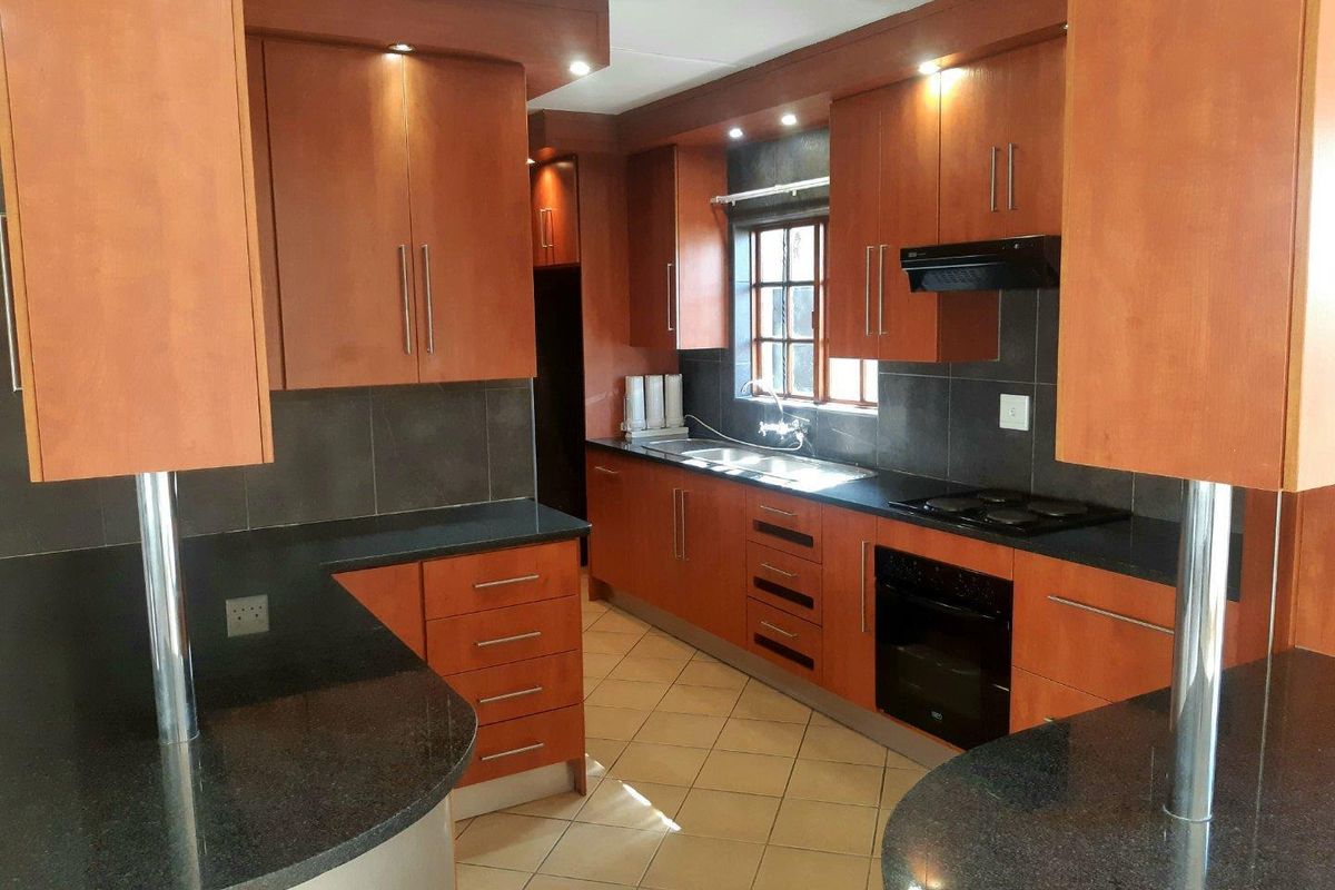 A functional kitchen featuring warm-toned wooden cabinetry, dark granite countertops, integrated appliances, and tiled flooring with ample storage space.