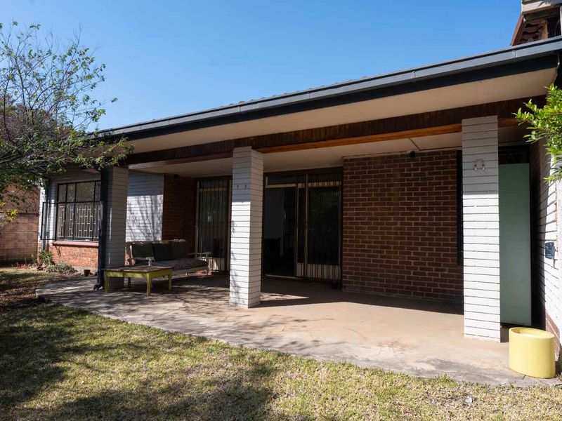 A covered outdoor patio area featuring brick pillars and direct access to the interior through sliding glass doors, overlooking the rear garden.