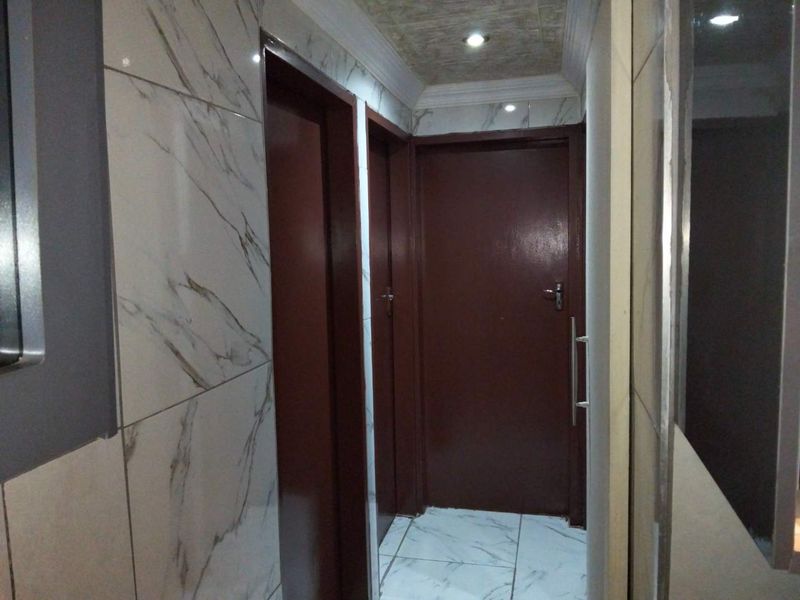 A clean, well-lit hallway featuring modern marble-look wall tiles, tiled flooring, and solid interior doors with recessed ceiling lighting.