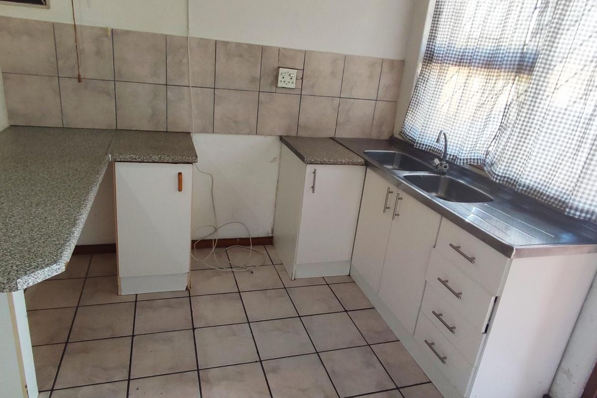 A functional kitchen area featuring laminate countertops, a double bowl stainless steel sink, tiled backsplash, and ceramic floor tiles with built-in base cabinetry.