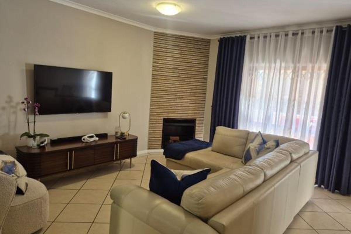 A comfortable living room featuring a stone-clad fireplace, tiled flooring, and large sliding doors with floor-to-ceiling curtains providing natural light.