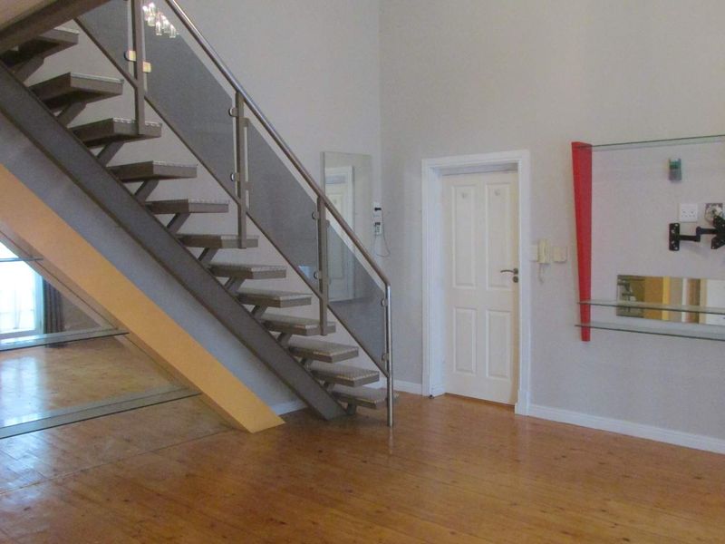 Open plan living area featuring a modern staircase with glass balustrades, wooden flooring, and a wall-mounted media display unit.
