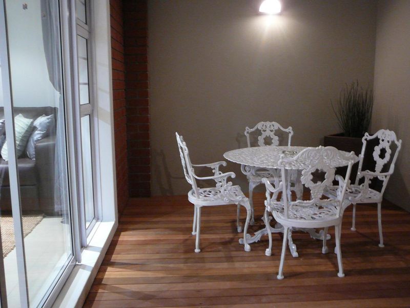 A covered patio area featuring timber decking, an exposed brick accent pillar, and a large sliding glass door providing access to the interior.