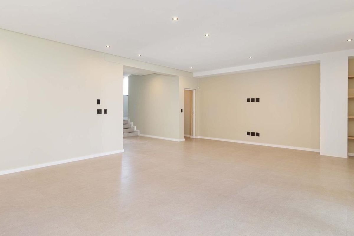 Spacious, open-plan living area featuring neutral tiled flooring, recessed downlighting, and built-in shelving, providing a clean and versatile space.