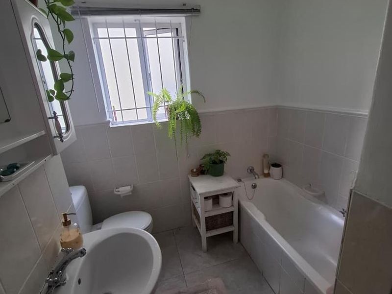 A functional bathroom featuring a pedestal basin, bathtub, and toilet with tiled finishes and a window with security bars.
