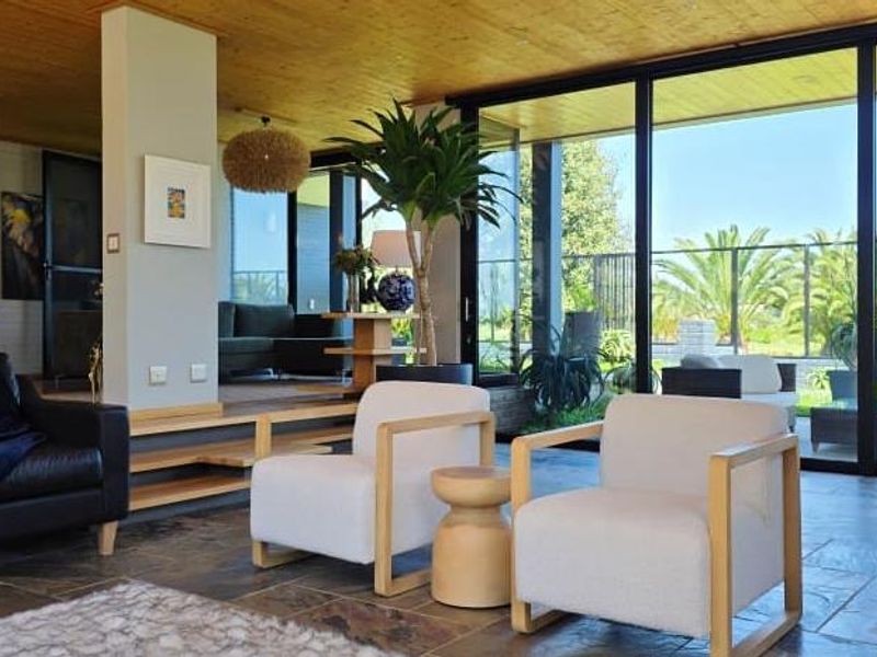 Spacious living area featuring natural timber ceilings, stone tile flooring, and expansive floor-to-ceiling sliding glass doors that provide seamless indoor-outdoor flow.