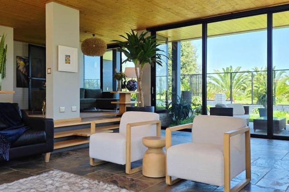 Spacious living area featuring natural timber ceilings, stone tile flooring, and expansive floor-to-ceiling sliding glass doors that provide seamless indoor-outdoor flow.