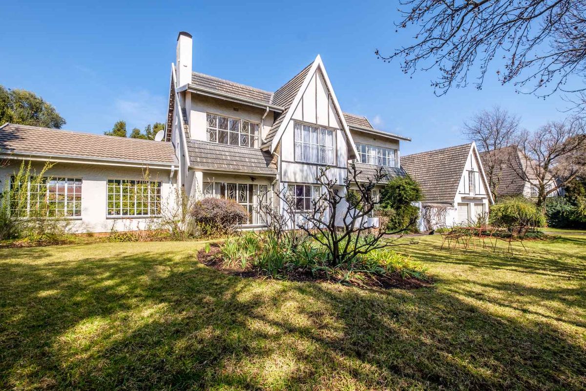 Rear view of a multi-story residence featuring a tiled roof, chimney, and large multi-pane windows set within a spacious garden.