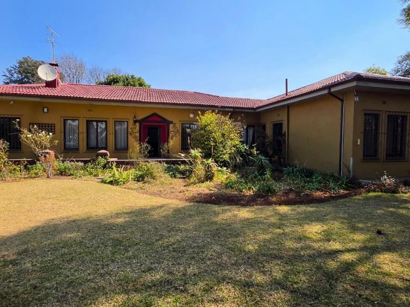 Rear view of a single-story house featuring a tiled roof, security bars on windows, and an established garden area.