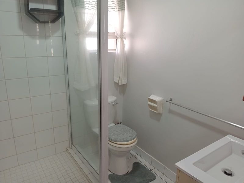 A functional bathroom featuring a glass-enclosed shower, a standard toilet, and a vanity basin with neutral wall finishes.