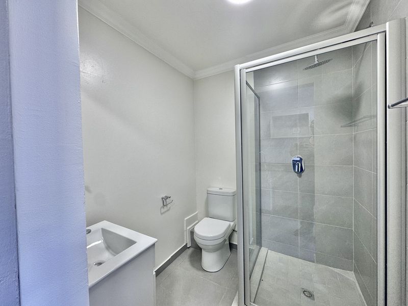 A clean and modern bathroom featuring a glass-enclosed shower, a contemporary toilet, and a vanity basin with neutral grey floor and wall tiling.