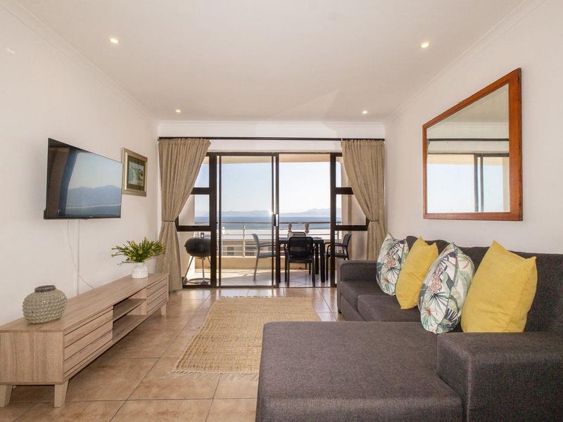 A bright living room featuring tiled floors, recessed lighting, and sliding glass doors that open onto a balcony with scenic views.