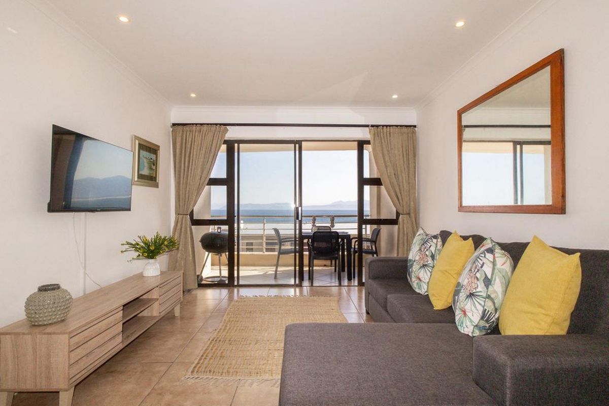 A bright living room featuring tiled floors, recessed lighting, and sliding glass doors that open onto a balcony with scenic views.