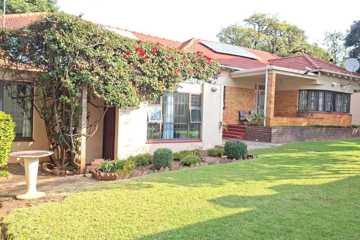 A well-maintained rear exterior view of a brick house featuring a terracotta tile roof, solar panels, and a spacious garden with a covered patio area.