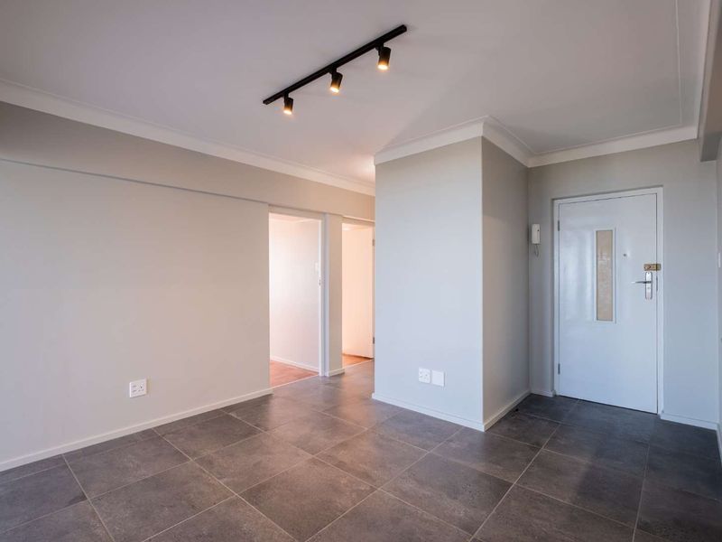 A clean and modern entrance hall featuring neutral walls, dark tiled flooring, and contemporary track lighting, providing a welcoming transition into the apartment.