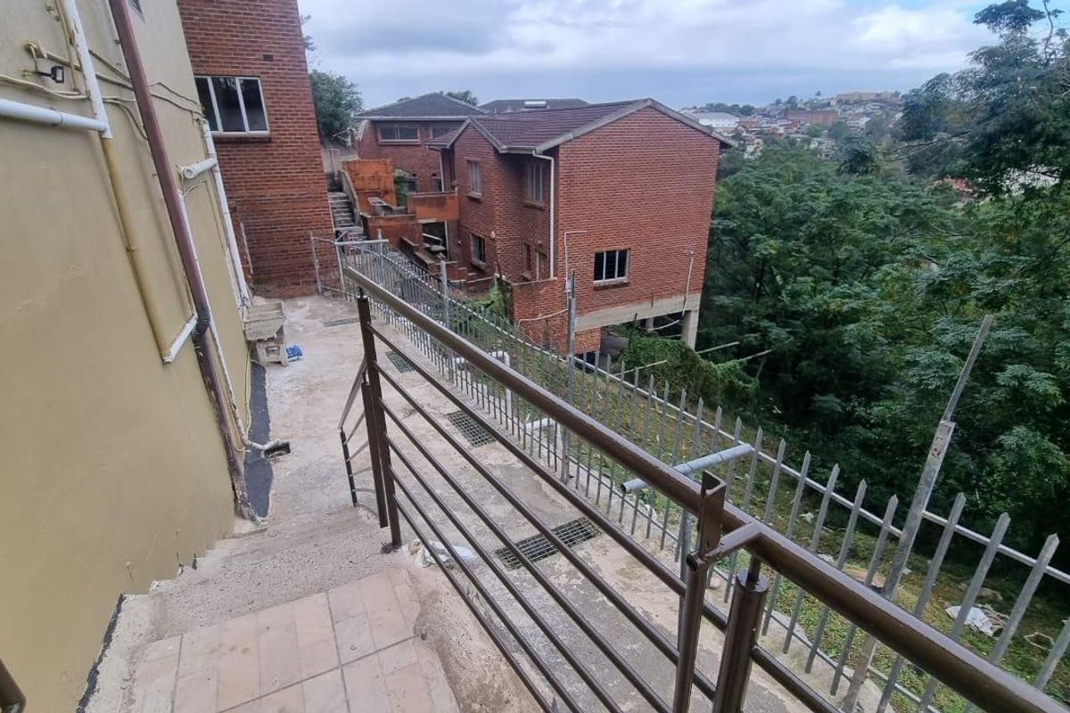 Rear exterior view showing concrete stairs, metal security fencing, and brick building facade with surrounding greenery.
