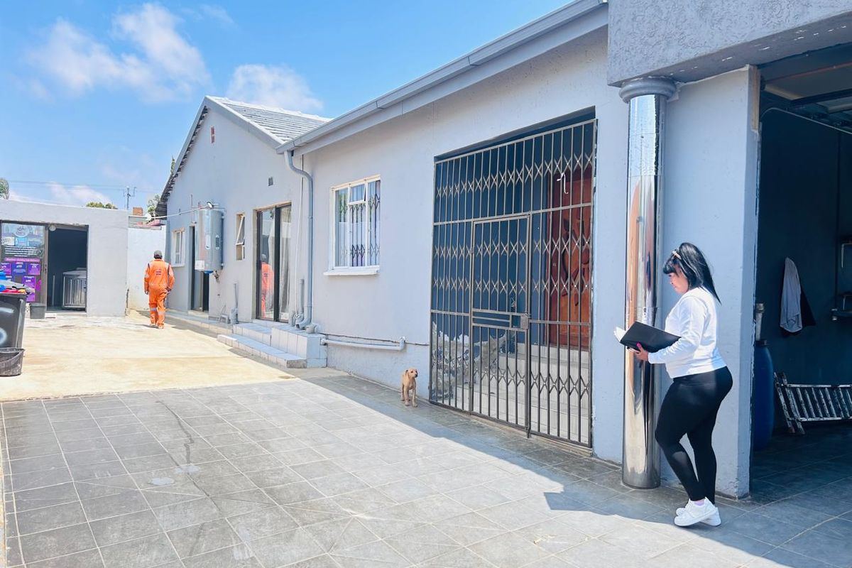 Rear exterior view of the property featuring a paved patio area, security gate, and external utility fixtures.