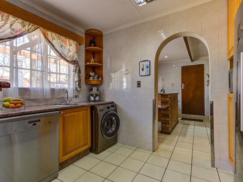 A functional scullery featuring tiled finishes, granite countertops, built-in cabinetry, and an arched entryway leading to the main living area.