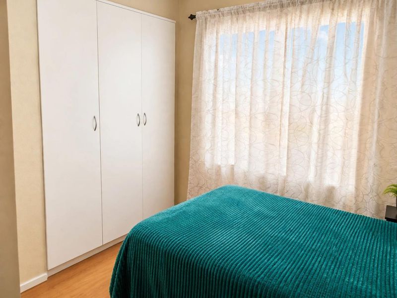 A well-maintained bedroom featuring light laminate flooring and a clean, white built-in wardrobe with ample storage space.
