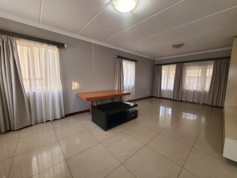 Spacious living room featuring large format floor tiles, neutral wall tones, and multiple windows with installed curtain tracks.