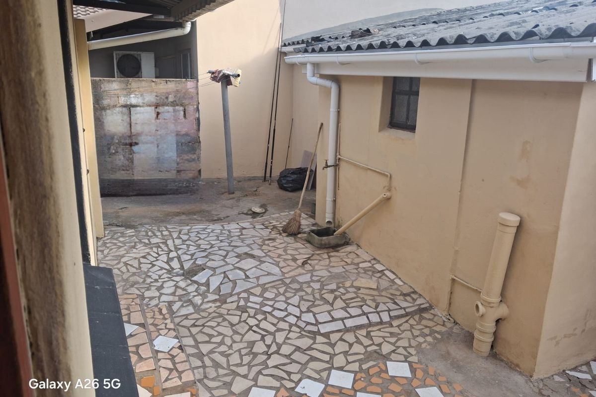 A rear courtyard area featuring crazy paving, external plumbing fixtures, and a corrugated roof structure, requiring maintenance and cosmetic updates.