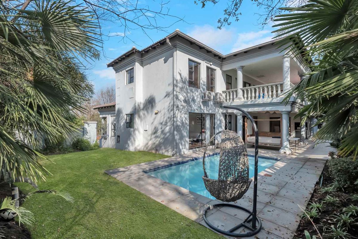 Rear view of a two-story residence featuring a swimming pool, covered patio with columns, and a landscaped garden area.