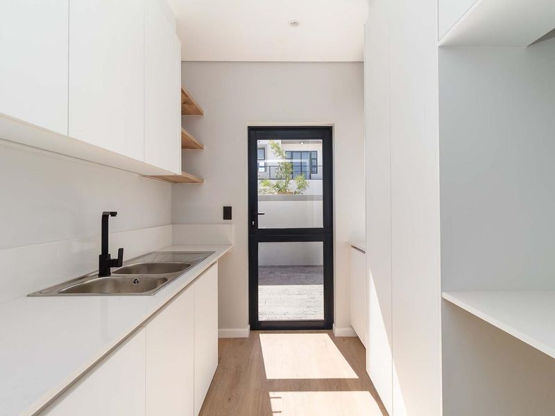 Modern scullery featuring sleek white cabinetry, stone countertops, a stainless steel double sink with black fixtures, and direct access to the exterior.