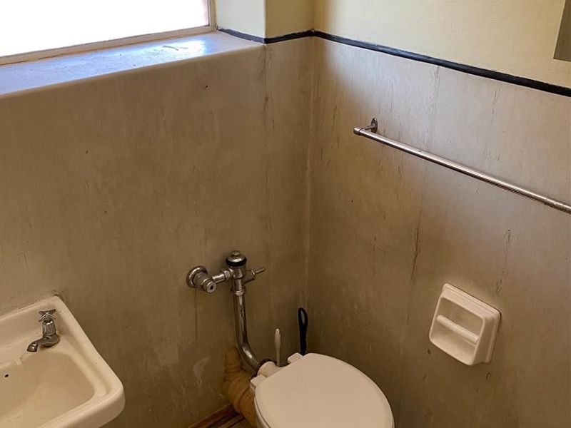 A compact bathroom featuring a wall-mounted basin and toilet, requiring cosmetic updates to the wall finishes and fixtures.