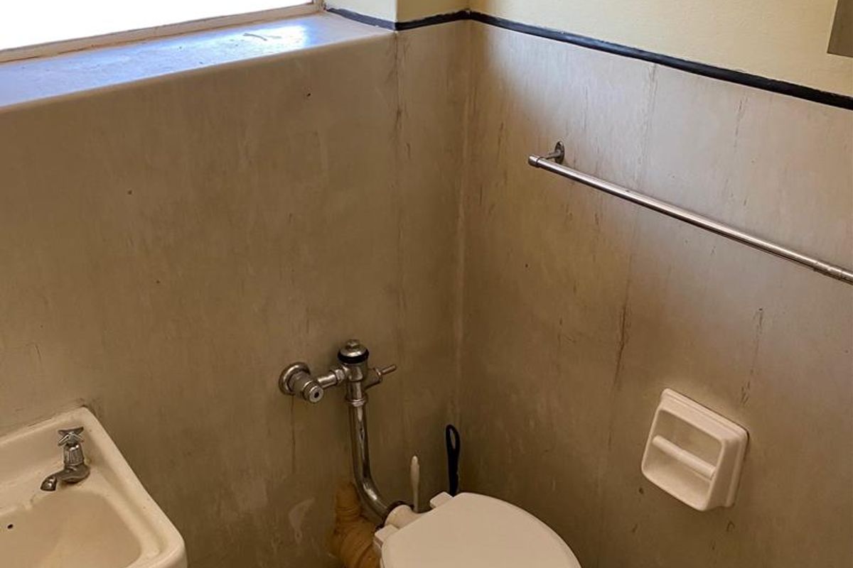 A compact bathroom featuring a wall-mounted basin and toilet, requiring cosmetic updates to the wall finishes and fixtures.
