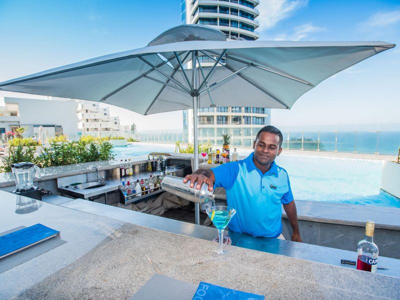 Outdoor pool area featuring a modern built-in bar counter with integrated sink, overlooking the ocean with glass balustrade safety fencing.