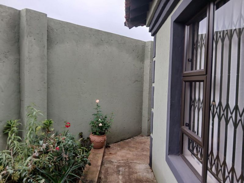 A side exterior view showing a concrete boundary wall, a paved walkway, and a window fitted with security bars.