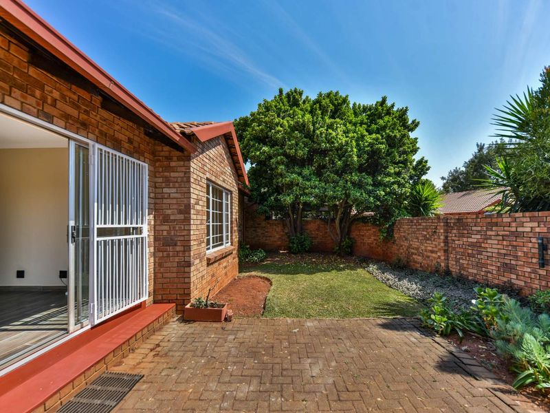 A private rear garden featuring a paved patio area, established trees, and a brick boundary wall, accessible via a sliding door with security gate.