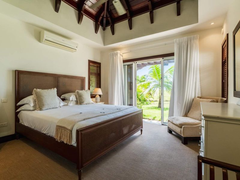 Spacious bedroom featuring a high vaulted timber ceiling, split-system air conditioning, and sliding glass doors opening to a private garden view.