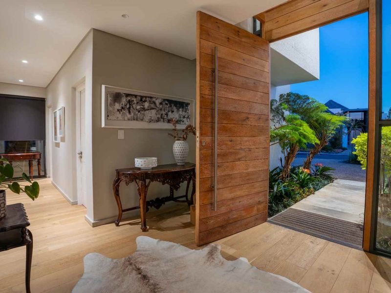 Modern entrance hall featuring a large timber pivot door, engineered wood flooring, and seamless transition to the outdoor garden area.