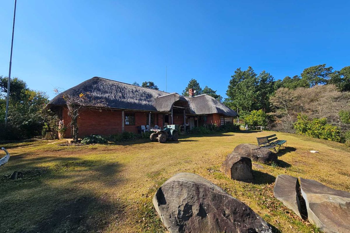 A rear view of a traditional farmhouse featuring a classic thatched roof and brick exterior, set within a spacious, landscaped garden area.