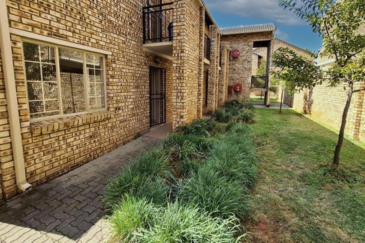Exterior view of a face brick apartment building featuring a paved walkway, landscaped garden area, and upper-level balconies.