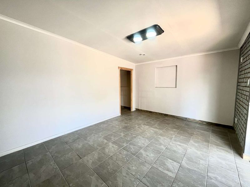 An empty living area featuring neutral ceramic floor tiles, an exposed brick accent wall, and a recessed wall niche, ready for personalization.