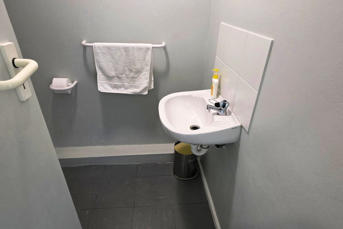 A compact office restroom featuring a wall-mounted ceramic basin, tiled splashback, and tiled flooring.