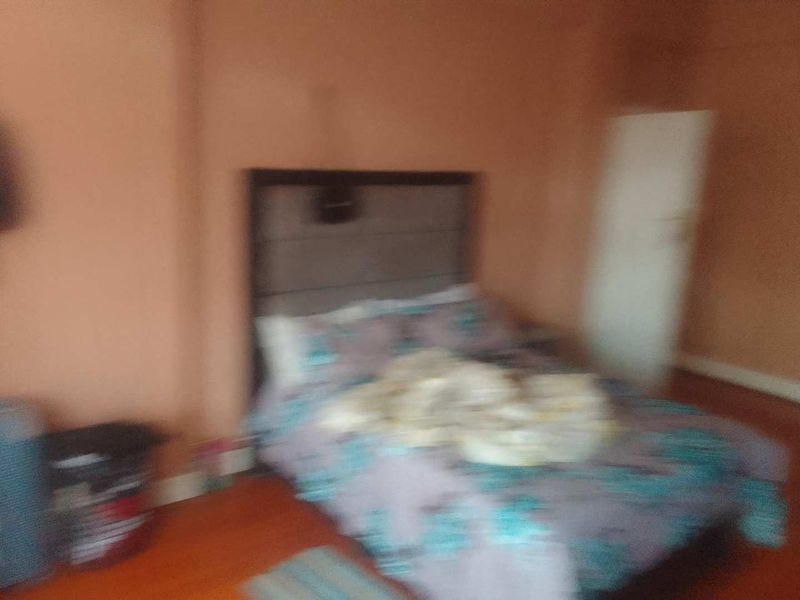 A bedroom featuring hardwood flooring and a standard door, currently in need of maintenance and better lighting.