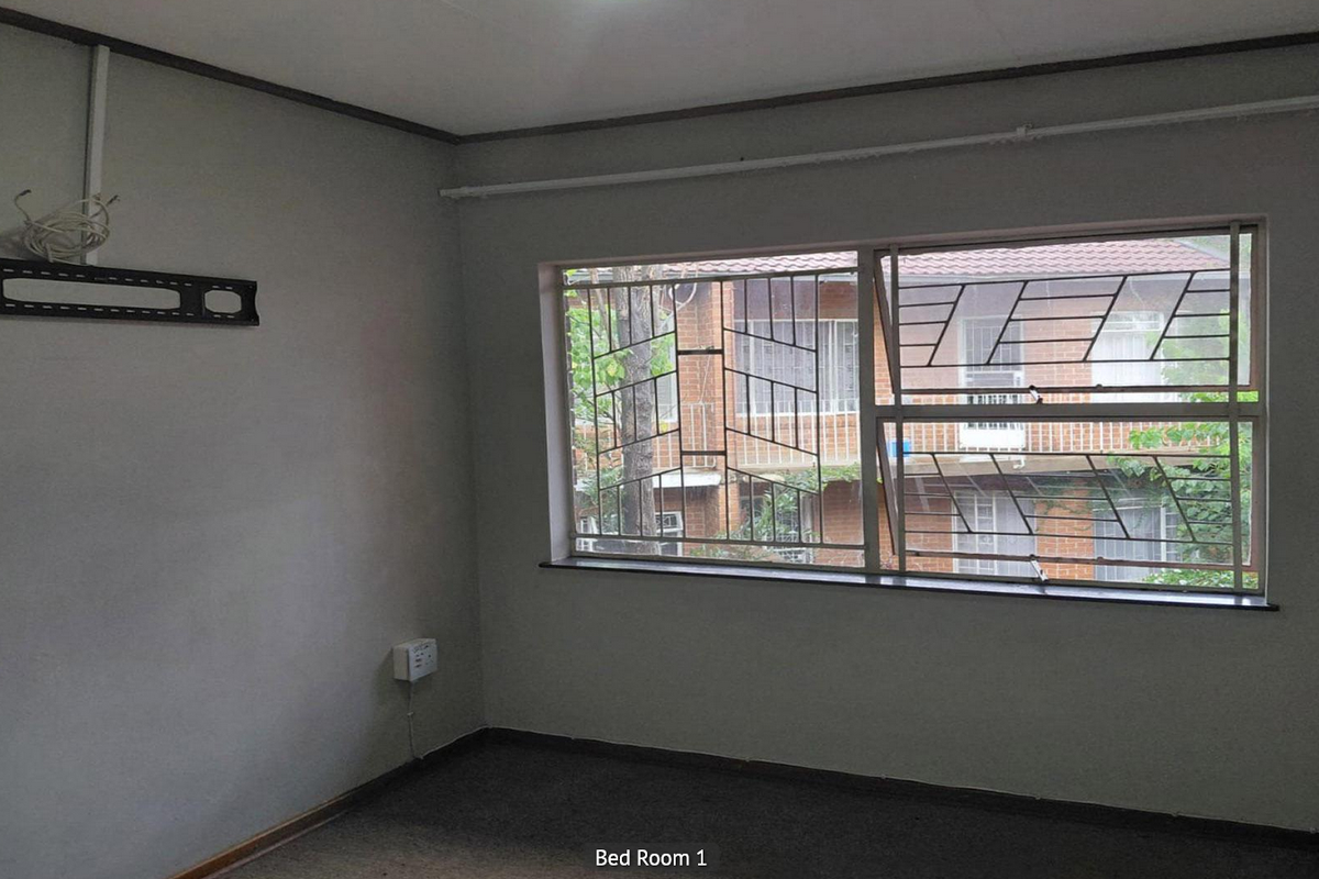 A vacant bedroom featuring carpeted flooring, a large window with security bars, and wall-mounted electrical and television bracket fixtures.