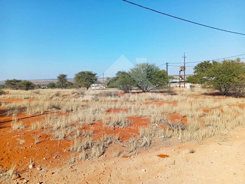 A view of a vacant residential plot featuring natural vegetation, red soil, and existing overhead utility infrastructure.