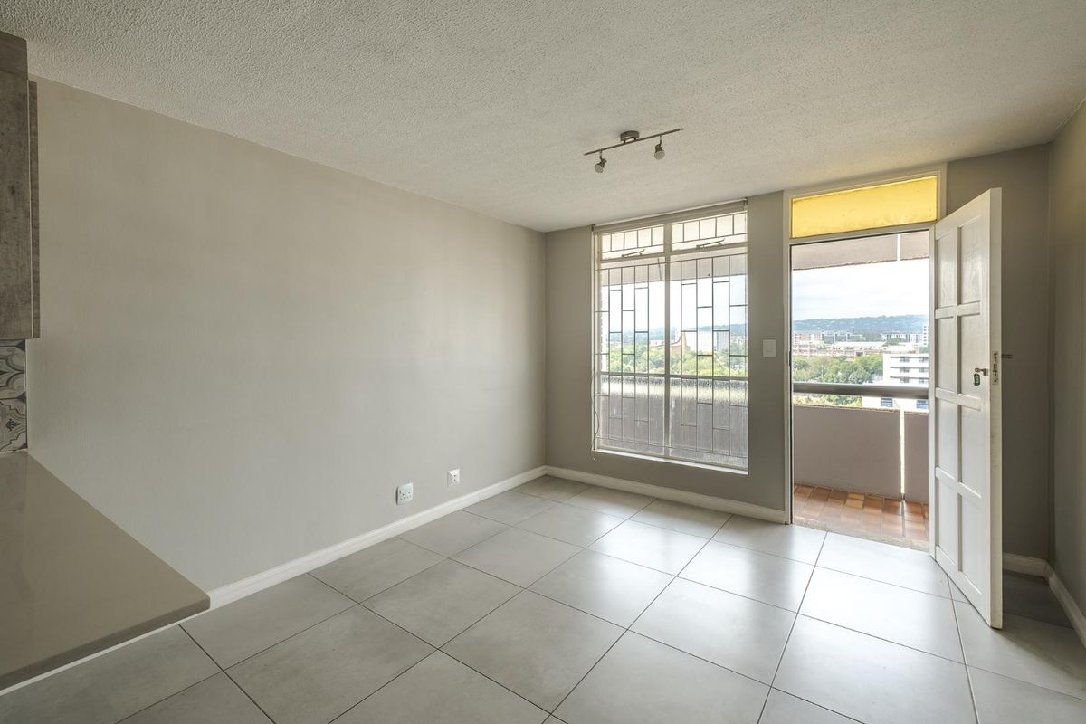 An empty living area featuring neutral tiled flooring, a security-grilled window, and direct access to a private balcony with urban views.