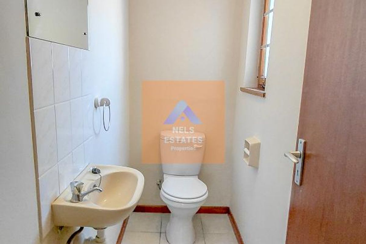 A compact guest bathroom featuring a wall-mounted basin, toilet, and neutral floor tiling, providing a functional and clean space.
