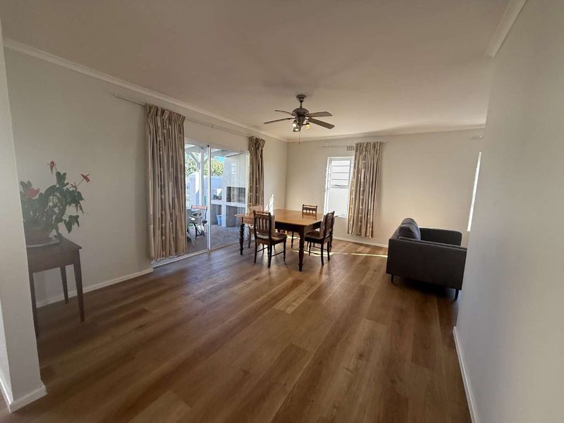 Spacious living and dining area featuring modern laminate flooring, a ceiling fan, and large sliding glass doors providing access to the outdoor patio.