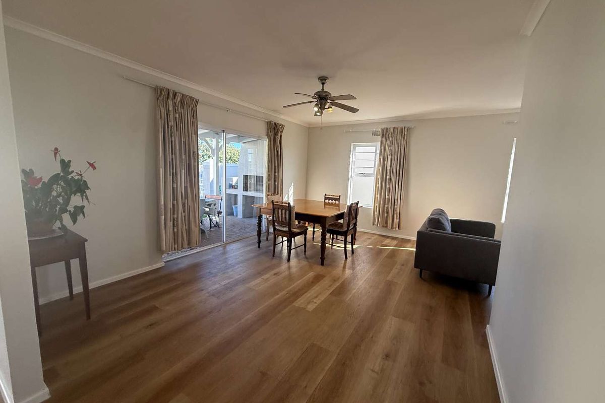 Spacious living and dining area featuring modern laminate flooring, a ceiling fan, and large sliding glass doors providing access to the outdoor patio.