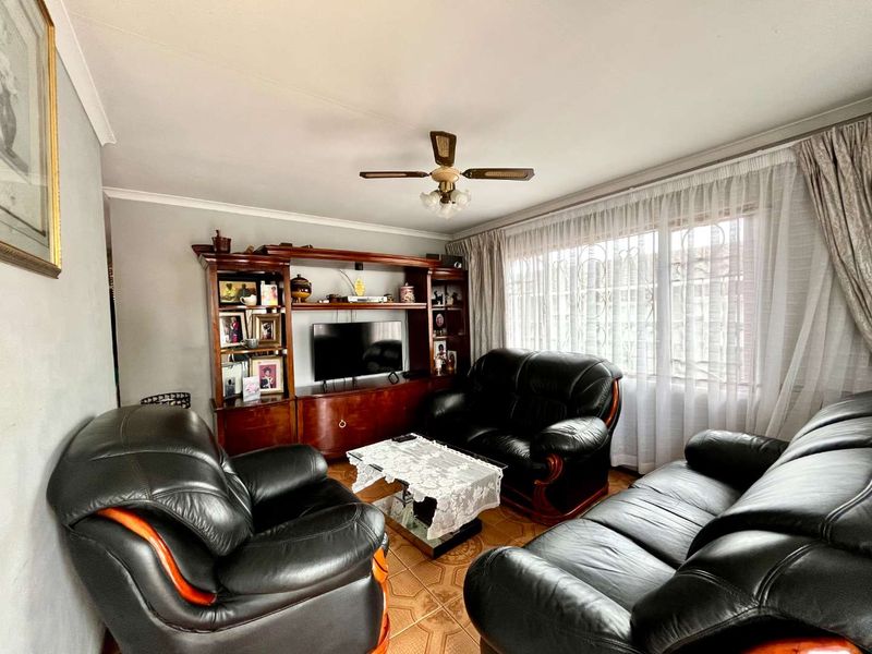 A living room featuring tiled flooring, a ceiling fan, and a large window with security bars.